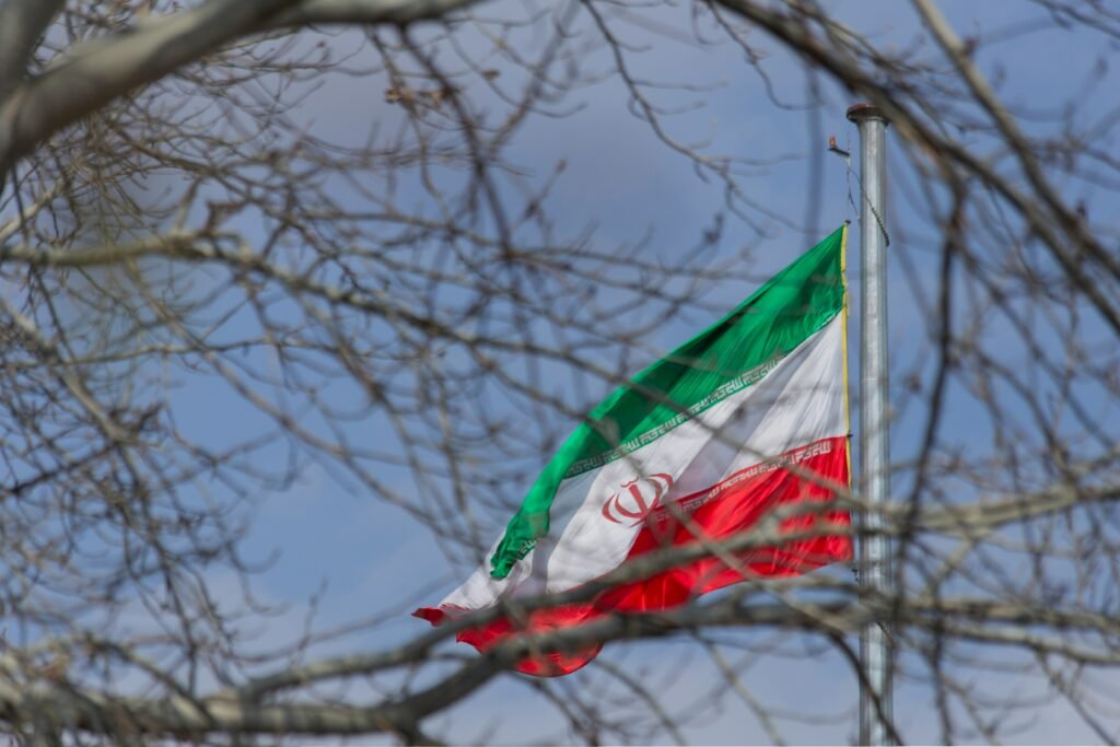 Iranian flag waving against a blue sky framed by tree branches
